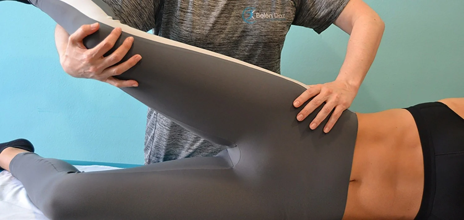 Fisioterapeuta movilizando la cadera de una paciente tumbada boca arriba, sujetando la rodilla flexionada